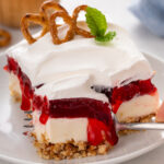 Slice of cherry pretzel salad on a white plate with a fork cutting a bite from the corner.