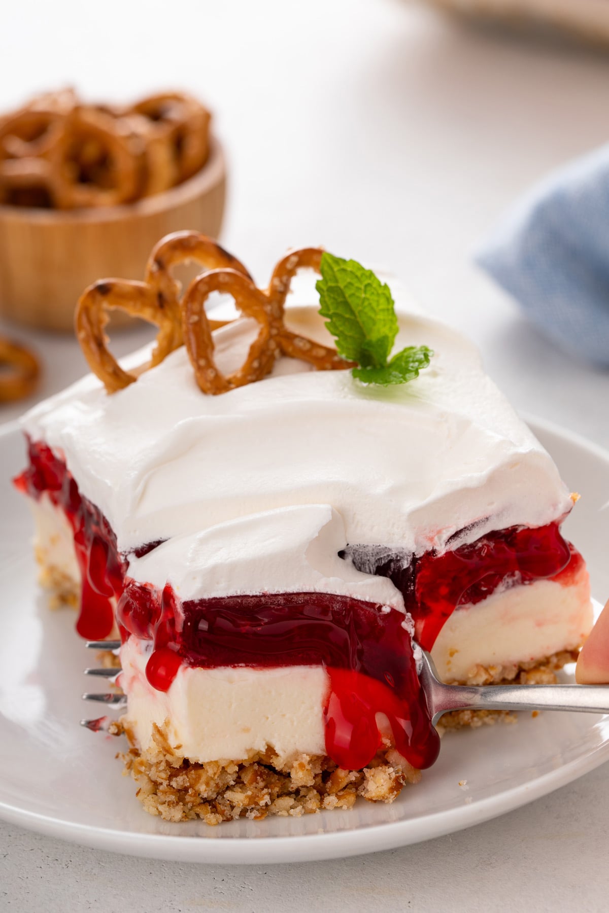 Fork cutting a bite from a corner of a plated slice of cherry cheesecake pretzel salad.