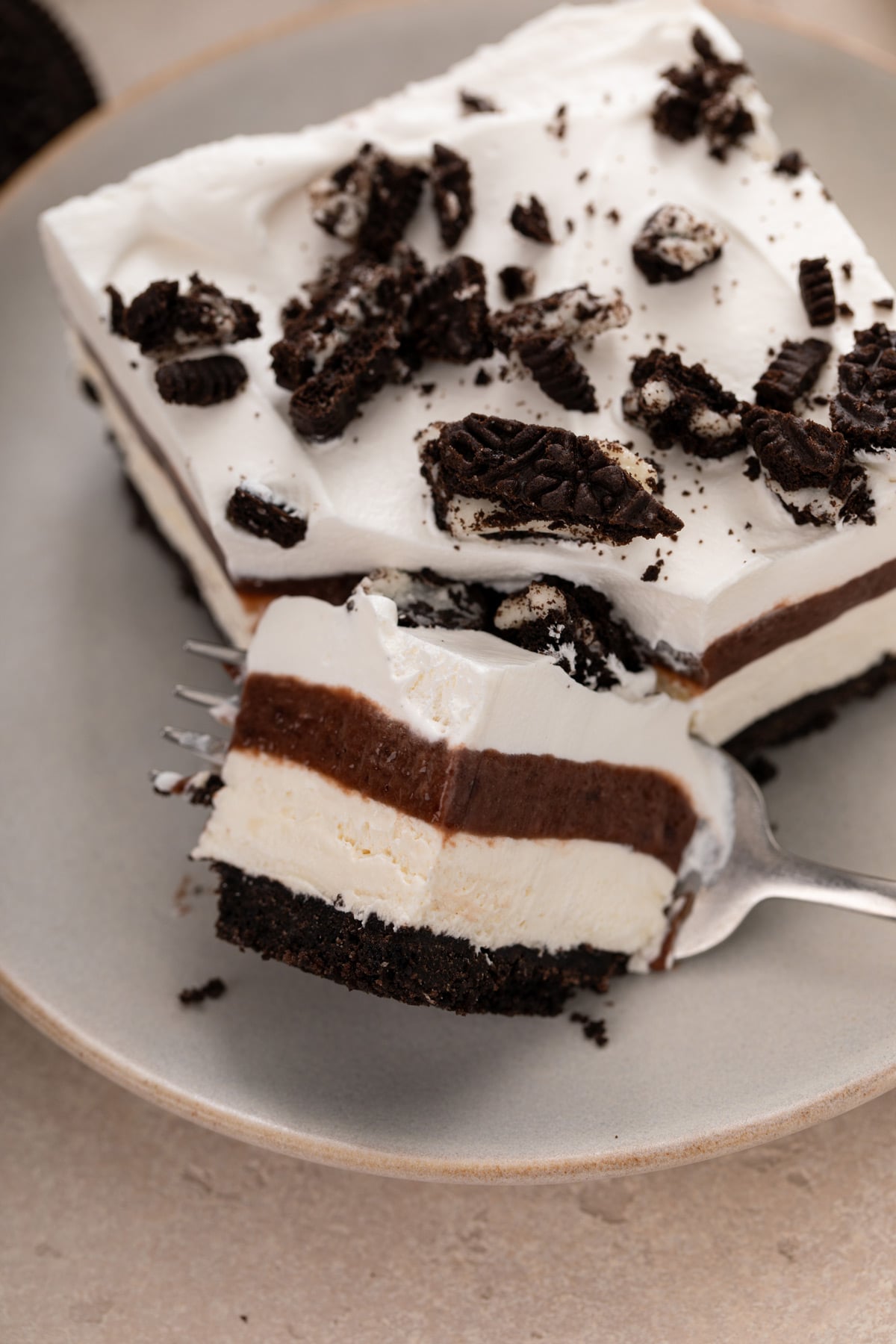 Fork cutting a bite from the corner of a plated slice of layered chocolate pudding dessert.