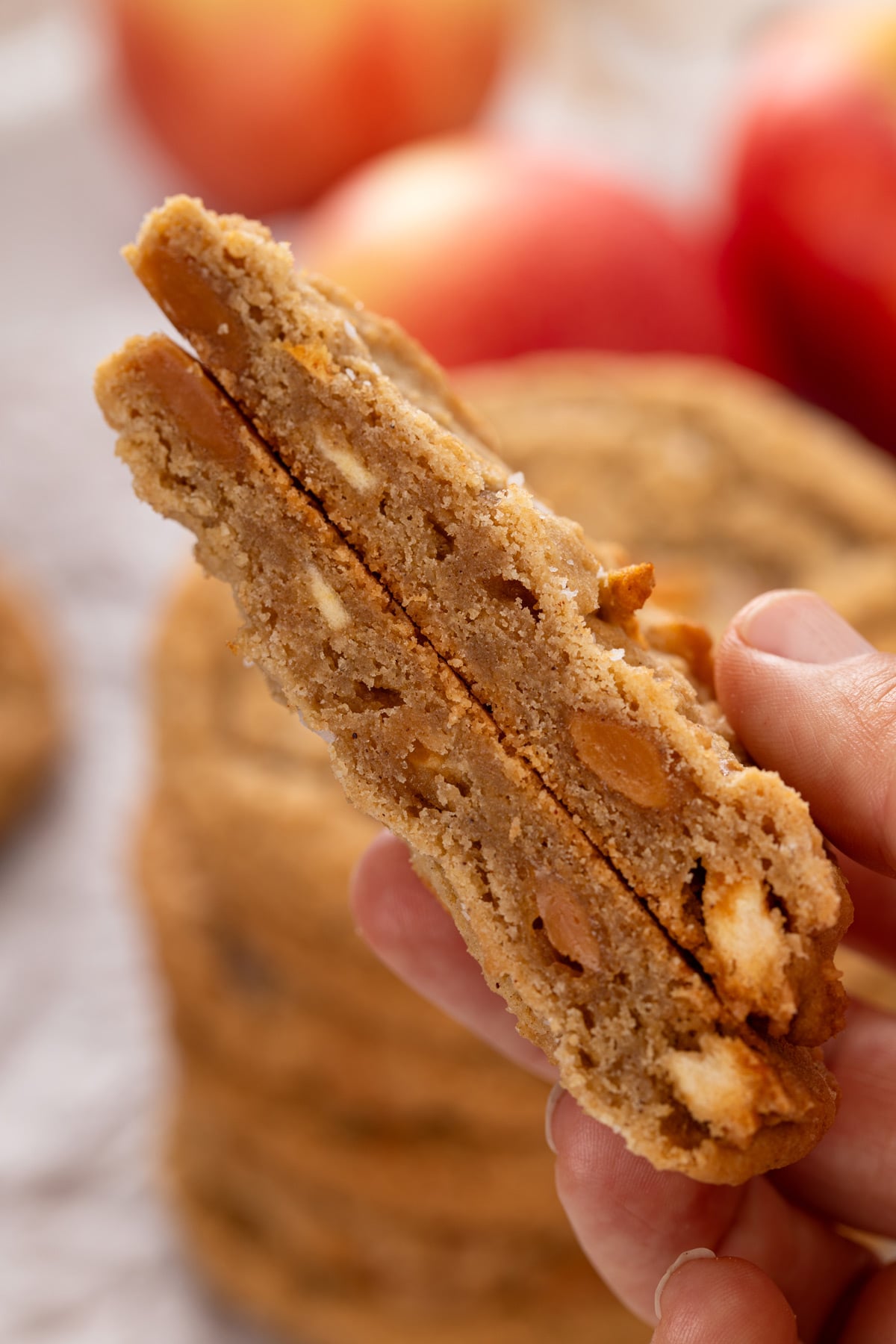 Hand holding up a halved caramel apple cookie to show the chewy inner texture.