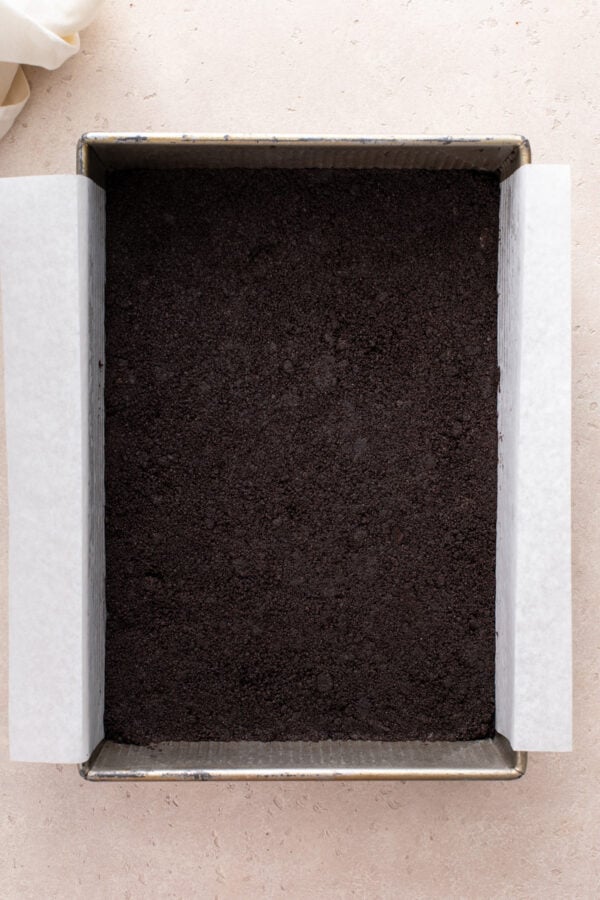 Oreo cookie crust pressed into a parchment-lined cake pan.