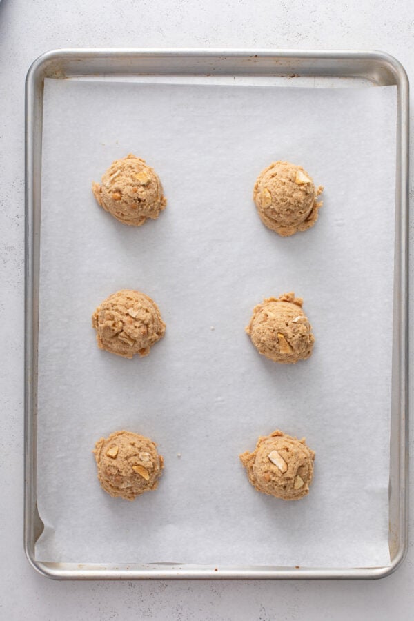 6 cookie dough balls for caramel apple cookies on a parchment-lined baking sheet.