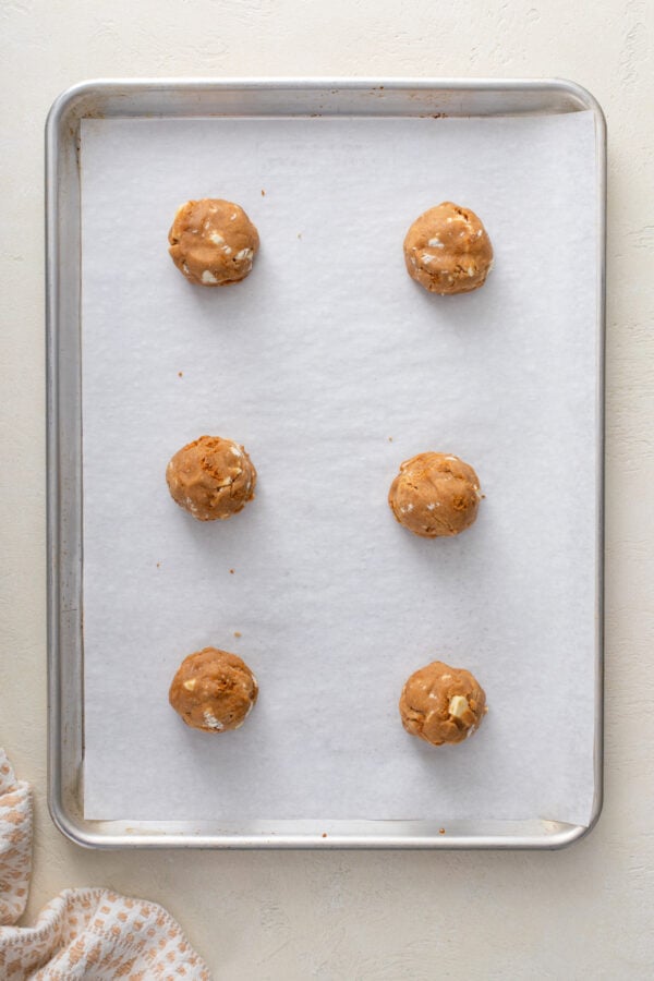 6 balls of cookie butter cookie dough arranged on a parchment-lined baking sheet.