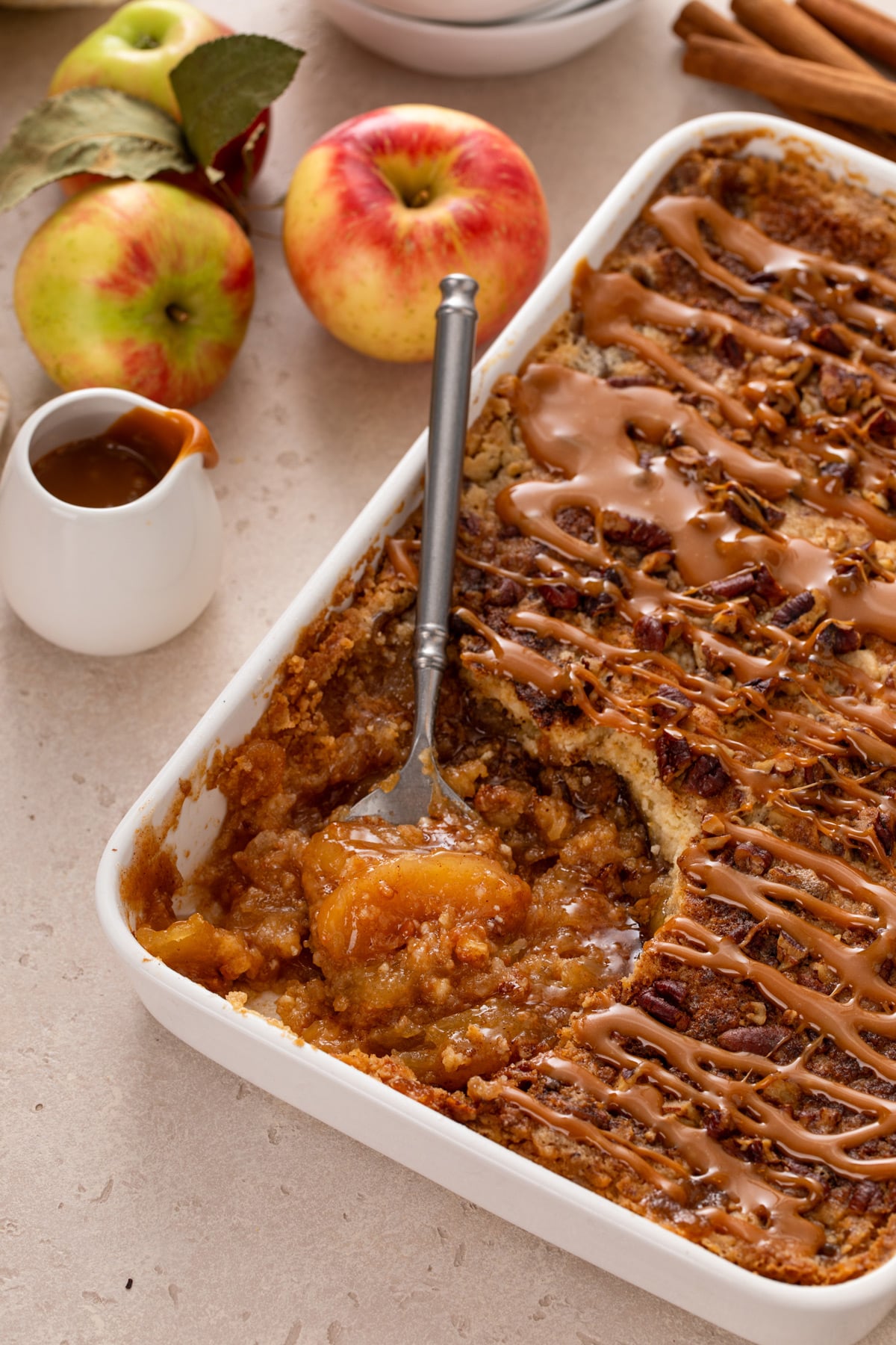 White baking dish filled with caramel apple dump cake with a serving spoon in the corner of the pan.