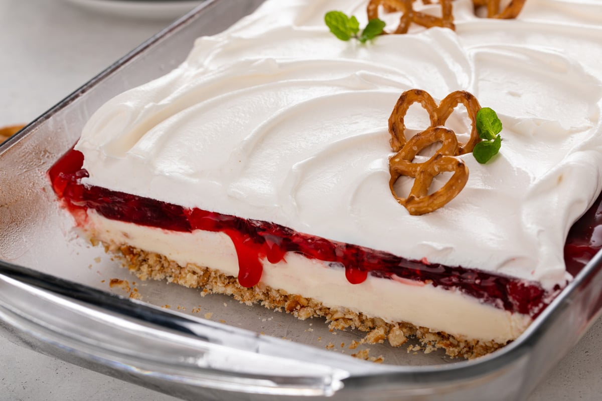 Cherry cheesecake pretzel salad in a glass pan with several slices removed to show the layers of the dessert.