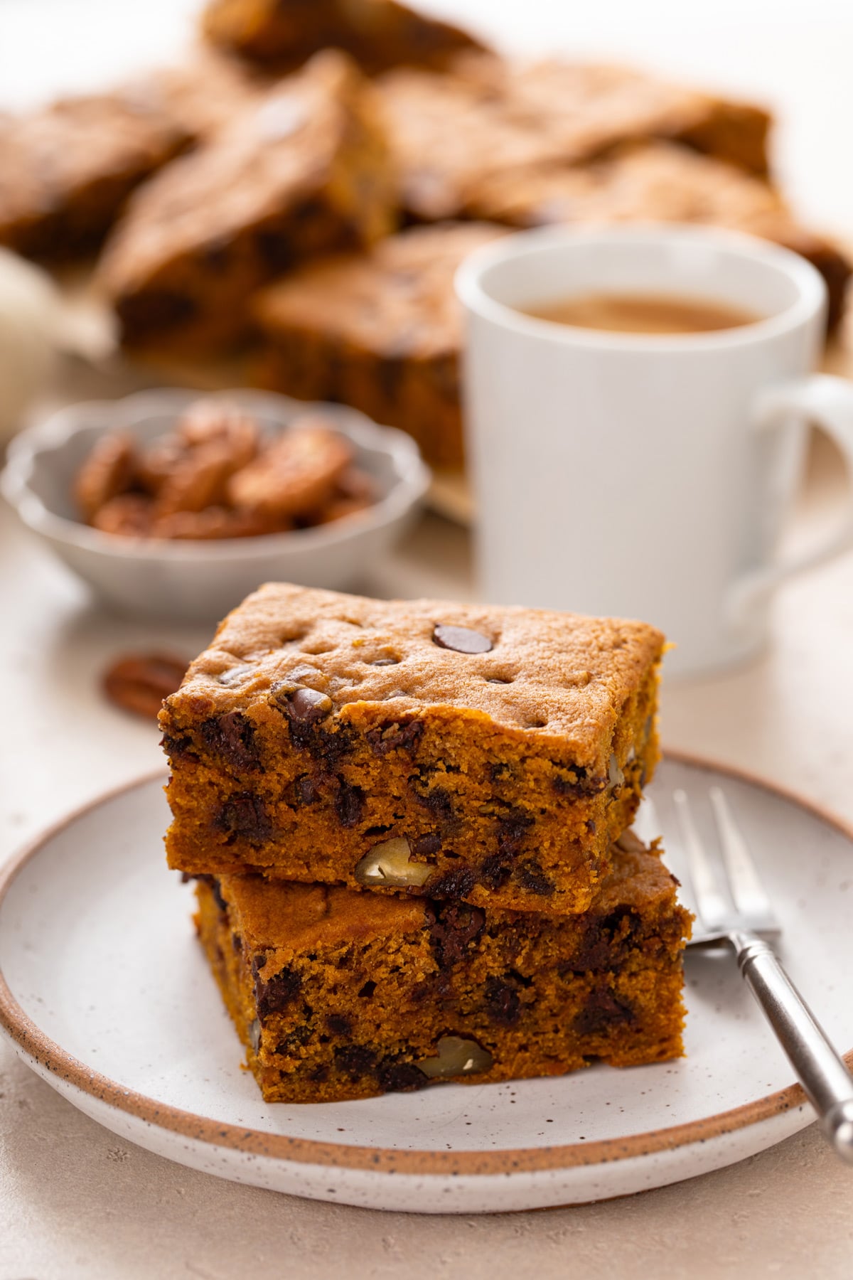 Two slices of pumpkin chocolate chip snack cake stacked on a plate in front of a cup of coffee.