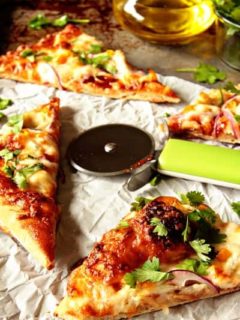 Four slices of BBQ chicken pizza next to a pizza cutter on a stone surface with baking paper