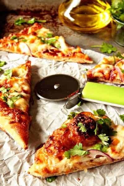 Four slices of BBQ chicken pizza next to a pizza cutter on a stone surface with baking paper