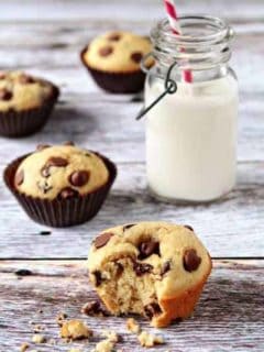 Chocolate chip muffin with a bite taken out of it in front of a glass of milk on a wood surface