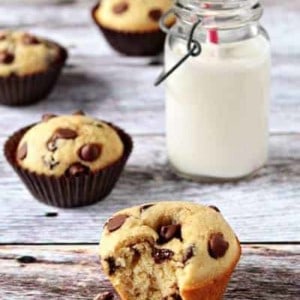 Chocolate chip muffin with a bite taken out of it in front of a glass of milk on a wood surface