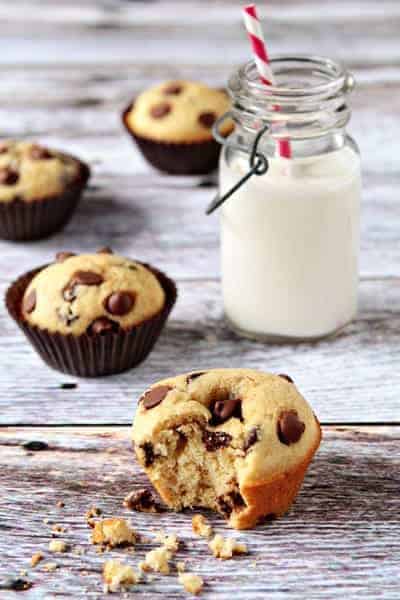 Chocolate chip muffin with a bite taken out of it in front of a glass of milk on a wood surface