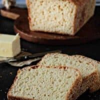 English muffin bread sliced on a black surface next to butter