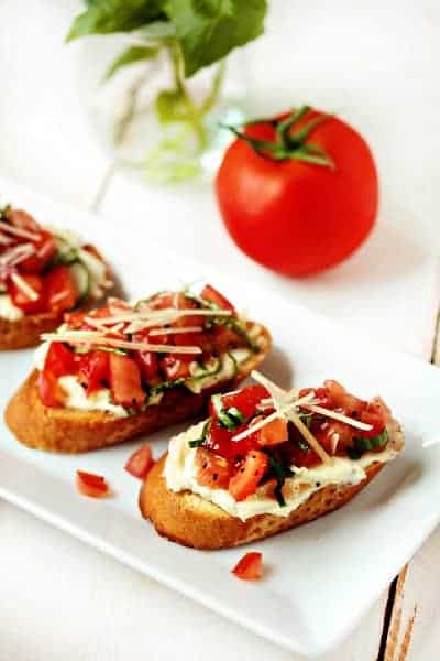 Three pieces of garlic tomato bruschetta on a white plate in front of a tomato