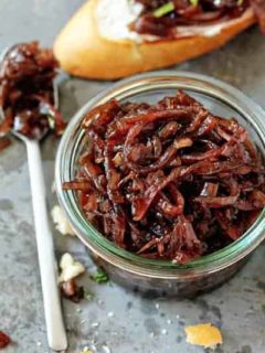 Glass jar full of red onion chutney next to a spoon
