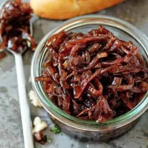 Glass jar full of red onion chutney next to a spoon