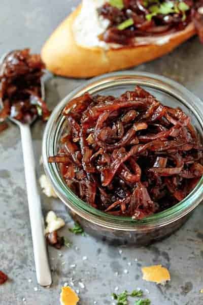 Glass jar full of red onion chutney next to a spoon
