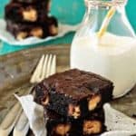 Two peanut butter Snickers brownies on a plate with a glass of milk