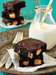 Two peanut butter Snickers brownies on a plate with a glass of milk