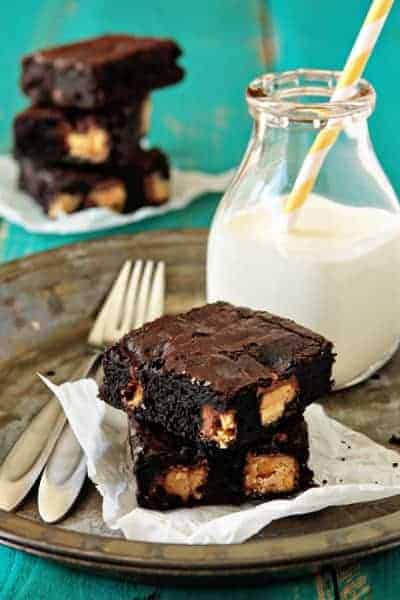Two peanut butter Snickers brownies on a plate with a glass of milk